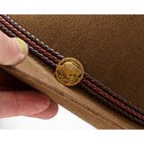 Close-up of a brown leather hat with braided band and copper color Buffalo emblem, held by a hand.
