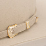 Close-up of a beige hat with a decorative gold and silver buckle.